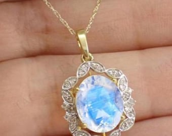 May include: A gold necklace featuring a pendant with a large, oval, blue and white moonstone. The moonstone is surrounded by a halo of small, clear gemstones set in a decorative, openwork frame. The chain is delicate.