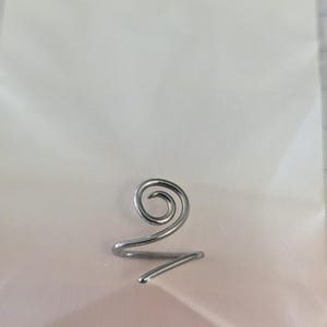 K&ouml;nnte beinhalten: Ein Ring aus silberfarbenem Metall, der aus einem einzigen durchgehenden Draht in Spiralform besteht. Der Draht biegt sich nach innen zu einer kreisf&ouml;rmigen Windung an der Oberseite, w&auml;hrend das restliche Ende eine einfache, offene Ringschiene bildet.