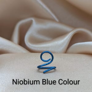 K&ouml;nnte beinhalten: Ein blauer Ohrring aus Niob mit einem spiralf&ouml;rmigen Drahtdesign. Der Metalldraht ist oben zu einer kreisf&ouml;rmigen Schlaufe geformt, die nach unten in ein spitzes Ende ausl&auml;uft. Der Text Niobium Blue Colour ist unter dem Schmuckst&uuml;ck abgedruckt.