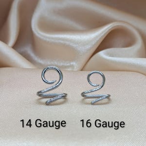 K&ouml;nnte beinhalten: Zwei spiralf&ouml;rmige Ohrklemmen oder Nasenringe aus silberfarbenem Metall. Das linke St&uuml;ck ist mit 14 Gauge und das rechte mit 16 Gauge beschriftet. Jeder Artikel verf&uuml;gt &uuml;ber ein kreisf&ouml;rmiges Spiraldesign, das in einem einzelnen Drahtende ausl&auml;uft.