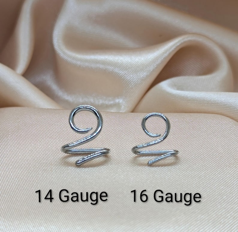 K&ouml;nnte beinhalten: Zwei spiralf&ouml;rmige Ohrklemmen oder Nasenringe aus silberfarbenem Metall. Das linke St&uuml;ck ist mit 14 Gauge und das rechte mit 16 Gauge beschriftet. Jeder Artikel verf&uuml;gt &uuml;ber ein kreisf&ouml;rmiges Spiraldesign, das in einem einzelnen Drahtende ausl&auml;uft.