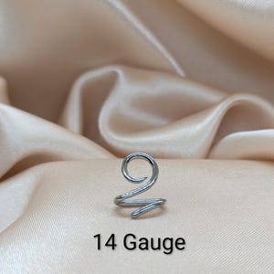 K&ouml;nnte beinhalten: Ein silberfarbener Ohrring aus Metall mit Spiraldesign. Das Schmuckst&uuml;ck ist mit 14 Gauge gekennzeichnet. Es besteht aus einem einzigen durchgehenden Draht, der sich oben zu einer Kreisform biegt und unten in einer kleineren Spirale endet.
