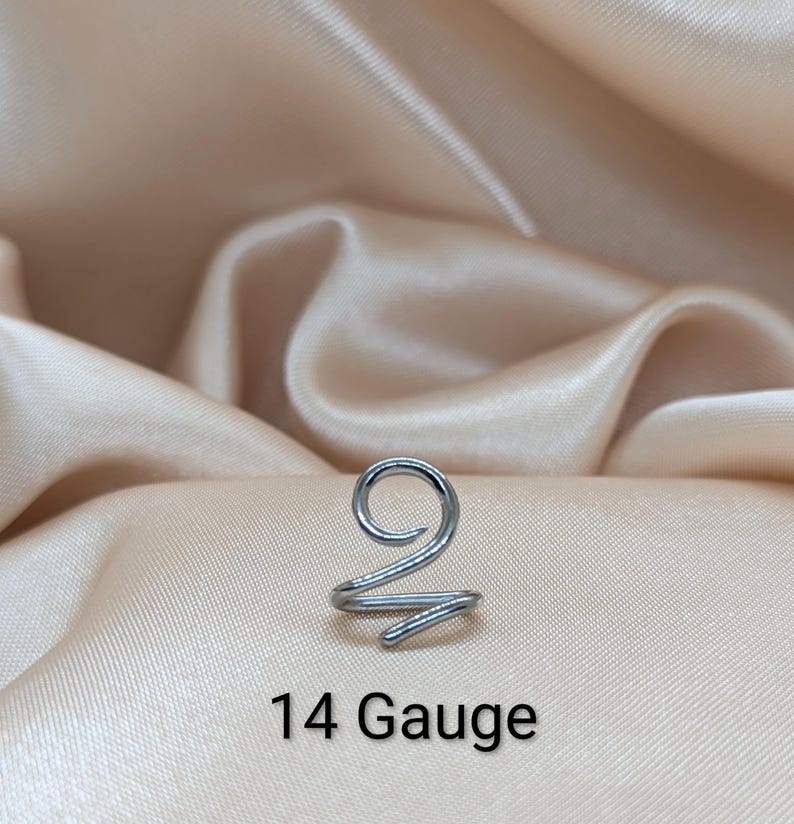 K&ouml;nnte beinhalten: Ein silberfarbener Ohrring aus Metall mit Spiraldesign. Das Schmuckst&uuml;ck ist mit 14 Gauge gekennzeichnet. Es besteht aus einem einzigen durchgehenden Draht, der sich oben zu einer Kreisform biegt und unten in einer kleineren Spirale endet.