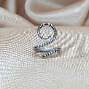 K&ouml;nnte beinhalten: Ein silberfarbener Ohrring aus Metall mit einem durchgehenden Spiraldesign. Das Schmuckst&uuml;ck besteht aus einem einzigen St&uuml;ck poliertem Draht, der sich oben zu einer kreisf&ouml;rmigen Schlaufe biegt und unten in einem geraden Ende ausl&auml;uft.