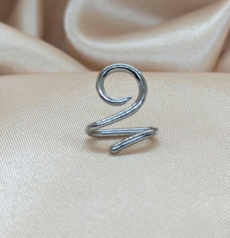 K&ouml;nnte beinhalten: Ein silberfarbener Ohrring aus Metall mit einem durchgehenden Spiraldesign. Das Schmuckst&uuml;ck besteht aus einem einzigen St&uuml;ck poliertem Draht, der sich oben zu einer kreisf&ouml;rmigen Schlaufe biegt und unten in einem geraden Ende ausl&auml;uft.