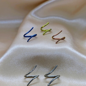 K&ouml;nnte beinhalten: F&uuml;nf einzelne Ohrklemmen in Form eines Blitzes oder Zickzacks. Das Set enth&auml;lt eine blaue, eine lindgr&uuml;ne, eine kupferfarbene und zwei silberfarbene Metallklemmen. Jedes St&uuml;ck hat ein schlichtes, durchgehendes Drahtdesign mit spitzen Enden.