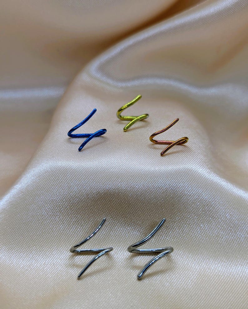 K&ouml;nnte beinhalten: F&uuml;nf einzelne Ohrklemmen in Form eines Blitzes oder Zickzacks. Das Set enth&auml;lt eine blaue, eine lindgr&uuml;ne, eine kupferfarbene und zwei silberfarbene Metallklemmen. Jedes St&uuml;ck hat ein schlichtes, durchgehendes Drahtdesign mit spitzen Enden.