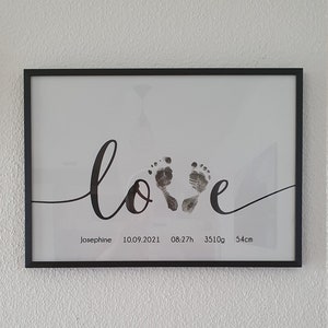 Könnte beinhalten: Ein schwarzer gerahmter Druck mit dem Wort "love" in Kursivschrift, wobei zwei Baby-Fußabdrücke im "o" zu sehen sind. Der Druck enthält außerdem den Namen "Josephine", das Datum "10.09.2021", die Uhrzeit "08:27h", das Gewicht "3510g" und die Länge "54cm".