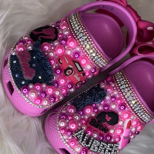 Puede incluir: Zapatos para ni&ntilde;os de color rosa y morado con tem&aacute;tica de Barbie. Los zapatos est&aacute;n decorados con diamantes de imitaci&oacute;n, perlas y un parche de mezclilla. Los zapatos tambi&eacute;n tienen el nombre "Aubree" escrito en ellos.