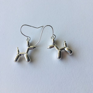 May include: A pair of silver balloon dog earrings. The earrings are made of metal and are shaped like balloon dogs. The earrings are hanging from silver hooks.