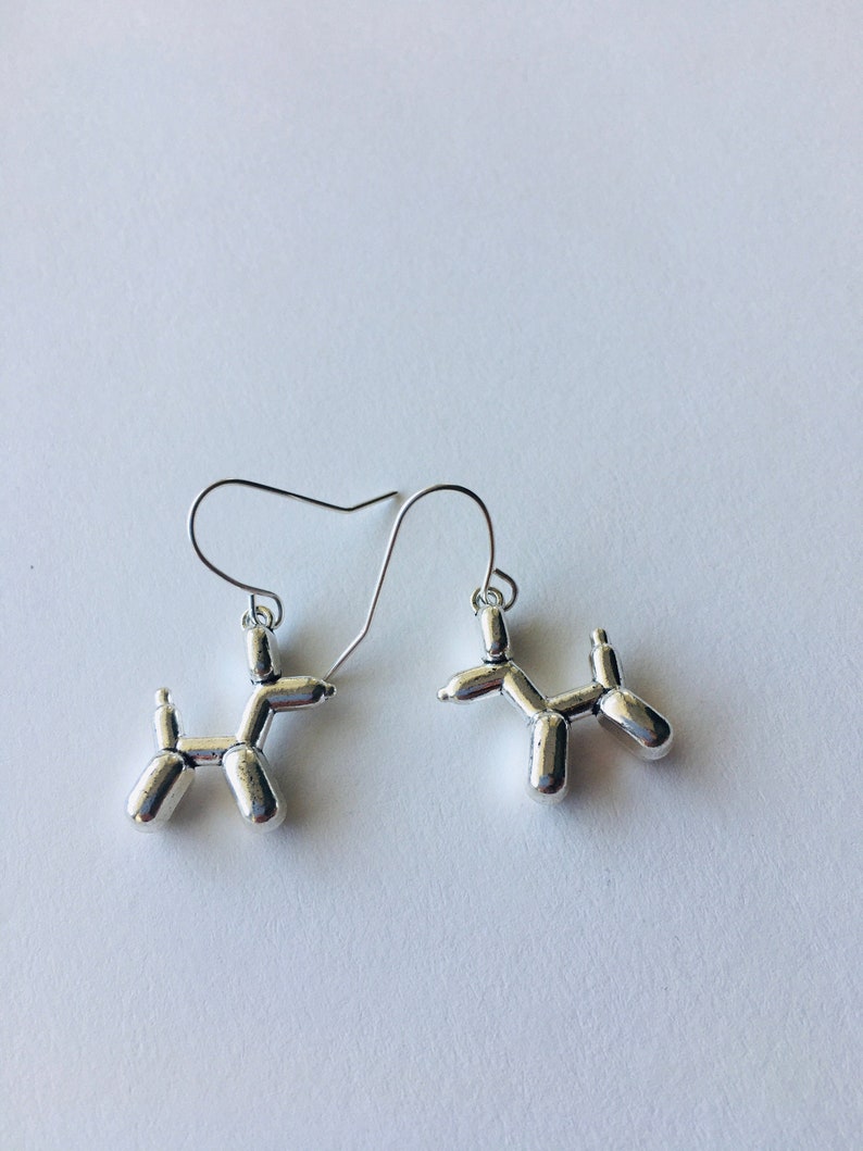 May include: A pair of silver balloon dog earrings. The earrings are made of metal and are shaped like balloon dogs. The earrings are hanging from silver hooks.