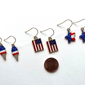 May include: A set of six patriotic earrings featuring red, white, and blue stars, flags, and ice cream cones. The earrings are approximately the size of a US penny.