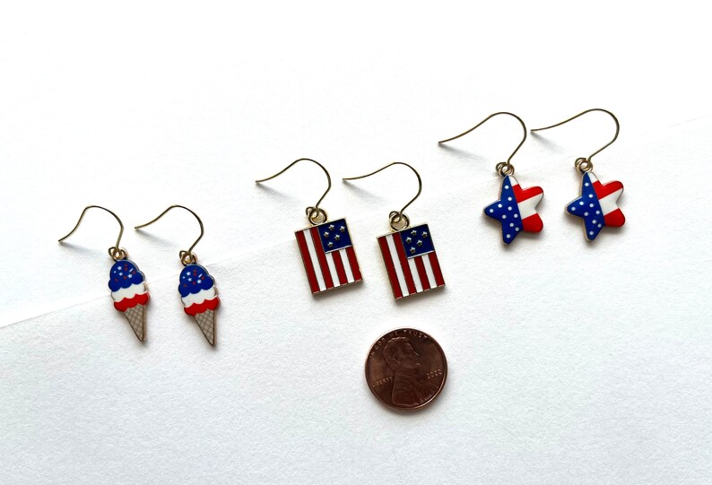 May include: A set of six patriotic earrings featuring red, white, and blue stars, flags, and ice cream cones. The earrings are approximately the size of a US penny.