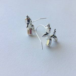 May include: A pair of silver balloon animal earrings. The earrings are shaped like a dog and a cat. The dog is silver with a gold accent. The cat is silver with a pink accent.