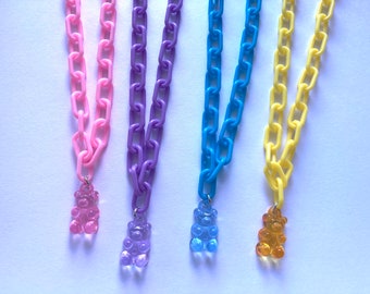 May include: Four necklaces with gummy bear charms. The necklaces are made of plastic chain links in pink, purple, blue, and yellow.