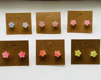 May include: Six pairs of star-shaped earrings on brown card stock. The earrings are made of translucent candy-like material in various colors, including pink, blue, yellow, and green.