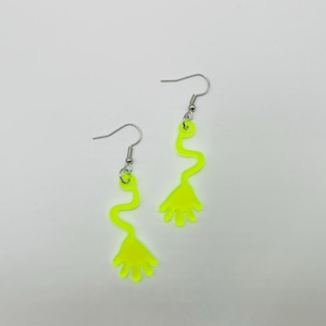 May include: A pair of neon yellow dangle earrings with a hand-shaped design at the bottom. The earrings have a silver hook.