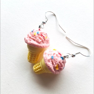 May include: A pair of pink ice cream cone earrings with colorful sprinkles. The earrings are made of polymer clay and have silver hooks.