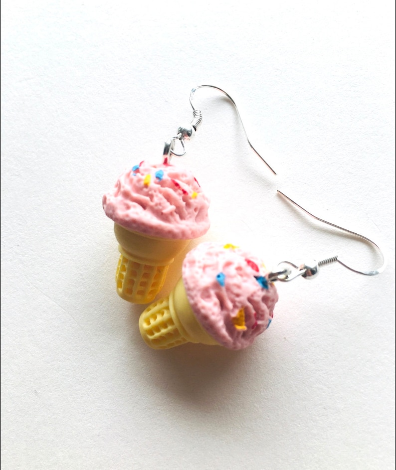 May include: A pair of pink ice cream cone earrings with colourful sprinkles. The earrings are made of polymer clay and have silver hooks.