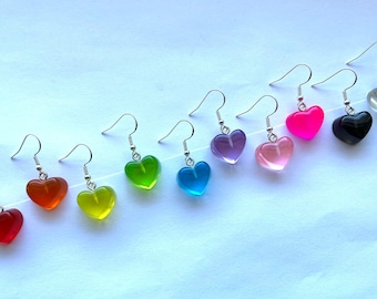 May include: A set of ten heart-shaped earrings in various colors, including red, orange, yellow, green, blue, purple, pink, black, clear, and white. The earrings are made of clear resin and have silver hooks.