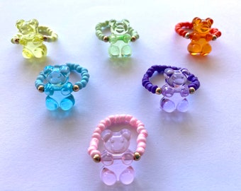 Peut inclure: Six bagues en forme d'ours en gomme de différentes couleurs : vert clair, bleu clair, violet, rose, orange et jaune. Chaque bague est ornée d'un charme en forme d'ours en gomme.