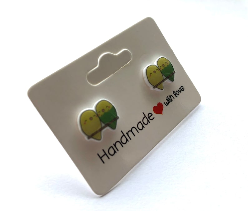 May include: A pair of green and yellow bird earrings on a white card with the text "Handmade with love".