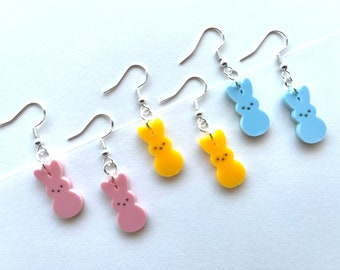 Peut inclure: Quatre paires de boucles d'oreilles pendantes avec des breloques en forme de lapin. Les breloques sont en résine rose pastel, jaune et bleue. Les boucles d'oreilles sont argentées.