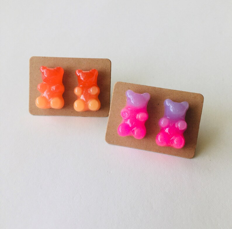 May include: Two pairs of gummy bear earrings. One pair is orange and yellow, the other is pink and purple.