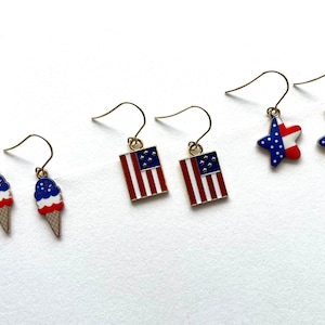 May include: A set of six patriotic earrings featuring American flag designs. Two pairs feature a red, white, and blue ice cream cone design, one pair features a red, white, and blue star design, and one pair features a red, white, and blue rectangle with stars.