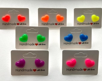 May include: Eight pairs of heart-shaped stud earrings displayed on white cards. The earrings are in various colors, including pink, red, orange, yellow, green, blue, and purple. Each card has the text "Handmade with love" printed on it.