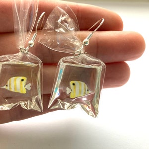 May include: A pair of earrings featuring a yellow and white butterfly encased in clear plastic. The butterflies are suspended from silver hooks.