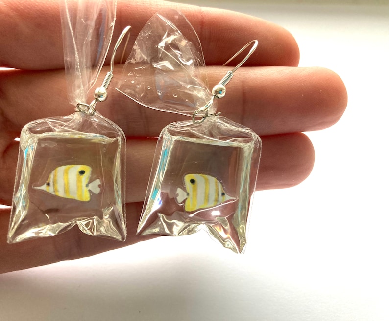 May include: A pair of earrings featuring a yellow and white butterfly encased in clear plastic. The butterflies are suspended from silver hooks.