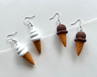 May include: A pair of earrings featuring ice cream cones. One pair is white soft serve ice cream and the other is chocolate ice cream.