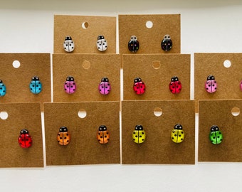 May include: Assortment of 10 pairs of ladybug stud earrings displayed on brown card stock. The earrings are in various colors including white, black, pink, red, orange, yellow, green, and blue.