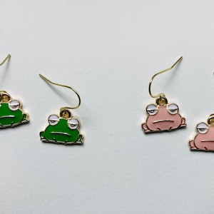 May include: A pair of gold frog earrings. One pair is green and the other is pink.