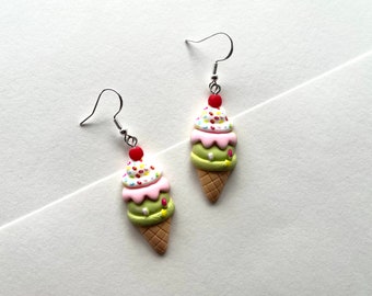May include: A pair of dangle earrings featuring a green, pink, and white ice cream cone with sprinkles and a red cherry on top.