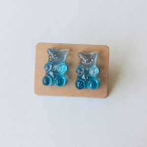 May include: A pair of blue gummy bear stud earrings with glitter accents.