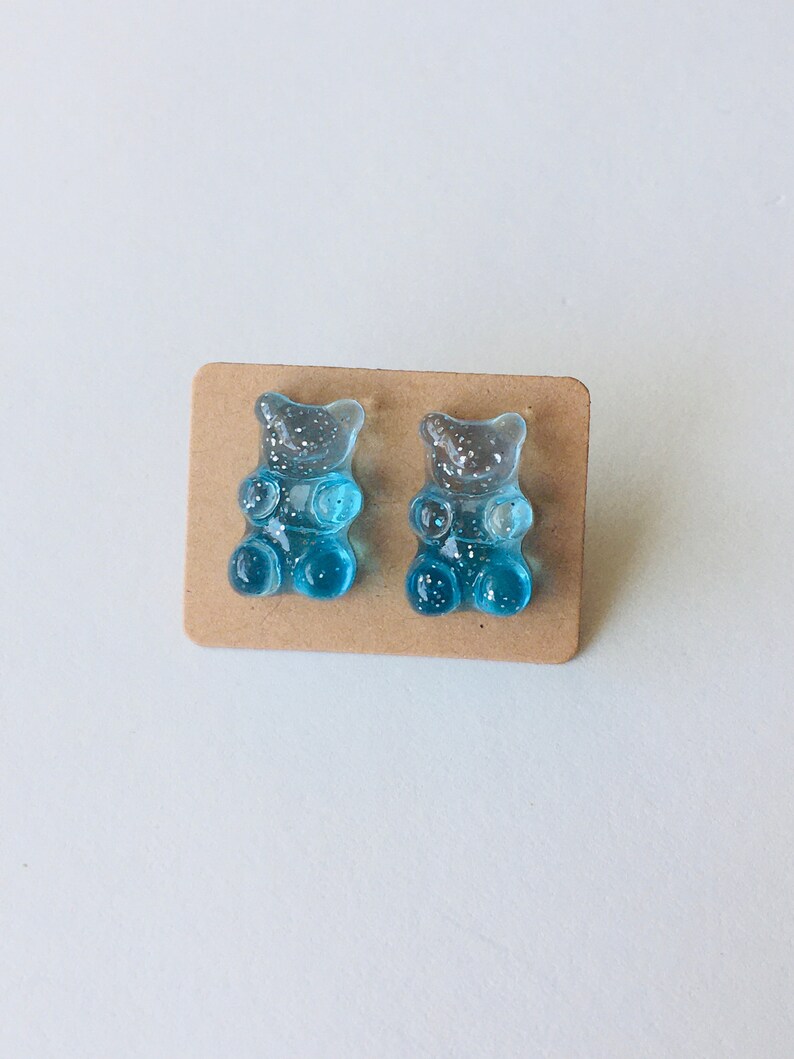 May include: A pair of blue gummy bear stud earrings with glitter accents.