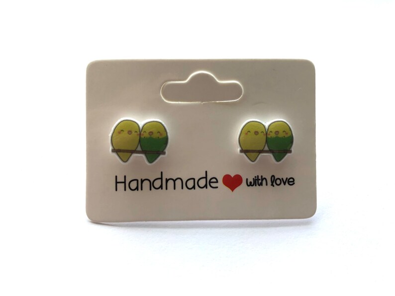 May include: A pair of green and yellow bird stud earrings on a white card with the text "Handmade with love".