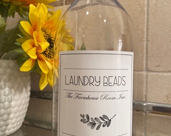 May include: Clear plastic bottle with a black lid, labeled "Laundry Beads The Farmhouse Room Inc." with a small leaf design. The label also states "Premium Quality" and "Net Wt. 64 oz."