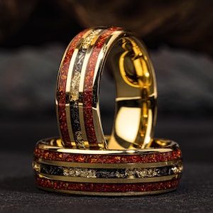 May include: Two gold rings with red and black inlay. The rings are stacked on top of each other.