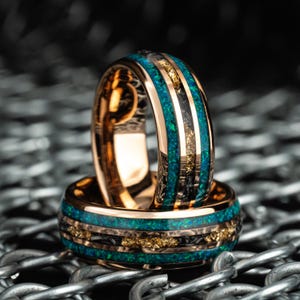 Puede incluir: Dos anillos de oro con incrustaciones negras y verdes. Los anillos están apilados uno encima del otro y tienen una banda dorada con incrustaciones negras y verdes.