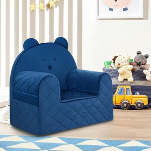 May include: A blue quilted armchair shaped like a bear with a bear face on the back. The chair is in a child's room with a basket of stuffed animals and a toy truck.
