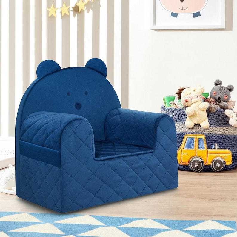 May include: A blue quilted armchair shaped like a bear with a bear face on the back. The chair is in a child's room with a basket of stuffed animals and a toy truck.