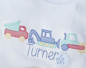 May include: A light blue sleeveless shirt with an embroidered design of construction vehicles and the name "Turner". The shirt is paired with red and white checkered shorts.
