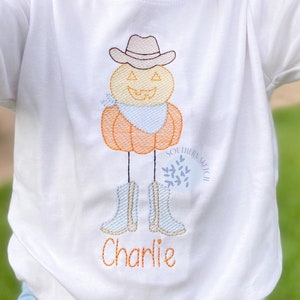 May include: White long-sleeve shirt with an embroidered pumpkin wearing a cowboy hat and boots. The pumpkin has a blue bandana and a smiling face. The text "SOUTHERN SAGE" and "Charlie" are embroidered on the shirt.