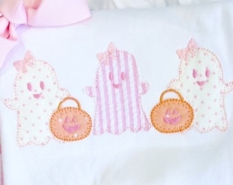 May include: A pink and white striped baby outfit with a white shirt featuring three embroidered ghosts holding jack-o'-lanterns. The outfit includes a pink and white striped bloomer.