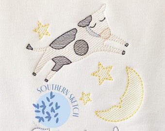 May include: White baby blanket with an embroidered design featuring a sleeping cow, yellow stars, and a crescent moon. The name "Judah" is embroidered in a cursive font below the design. The blanket has the text "SOUTHERN SKETCH" and a logo.