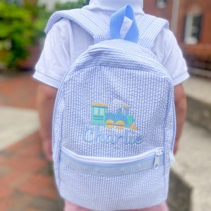 May include: A blue and white gingham backpack with a train and the name "Charlie" embroidered on the front.