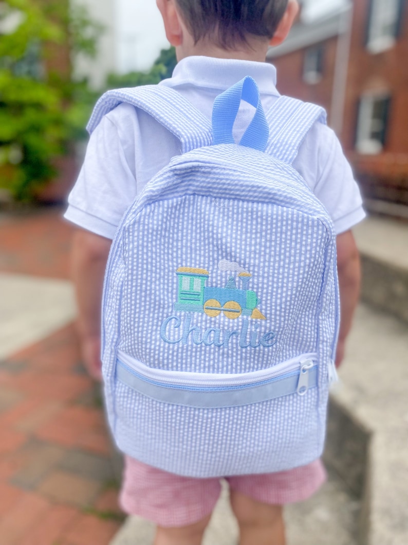 May include: A blue and white gingham backpack with a train and the name "Charlie" embroidered on the front.